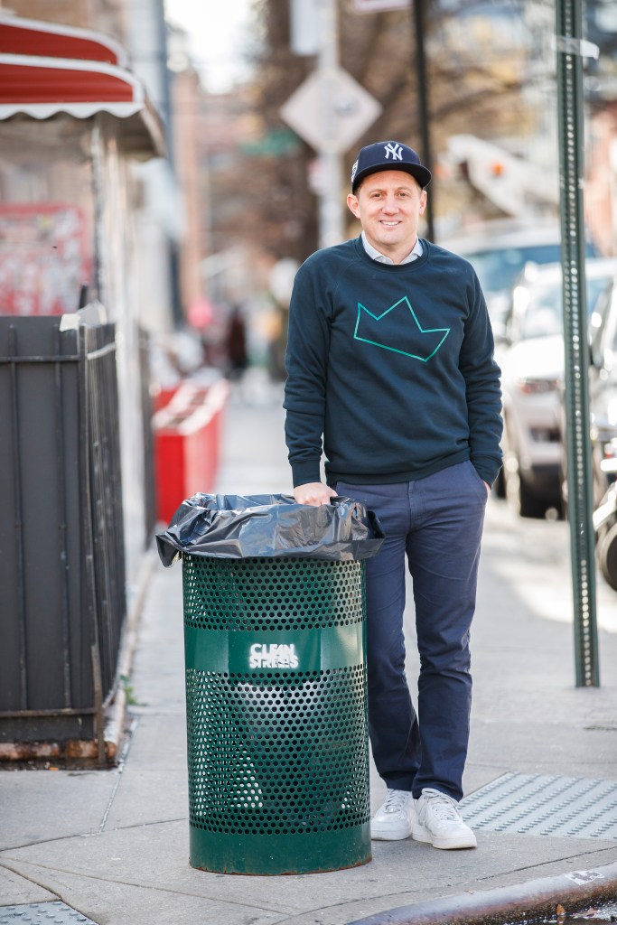 Sean Feeney standing on a corner in Williamsburg next to one of his garbage cans.