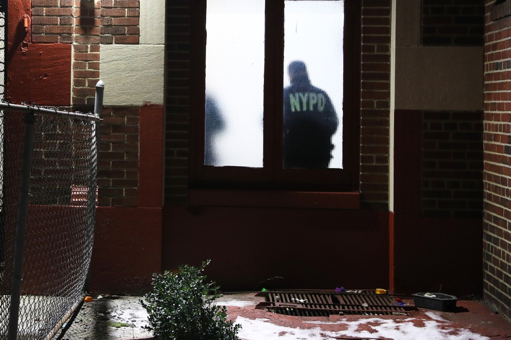 A NYPD officer stands inside the window of a Brooklyn apartment building with his back to the fogged glass