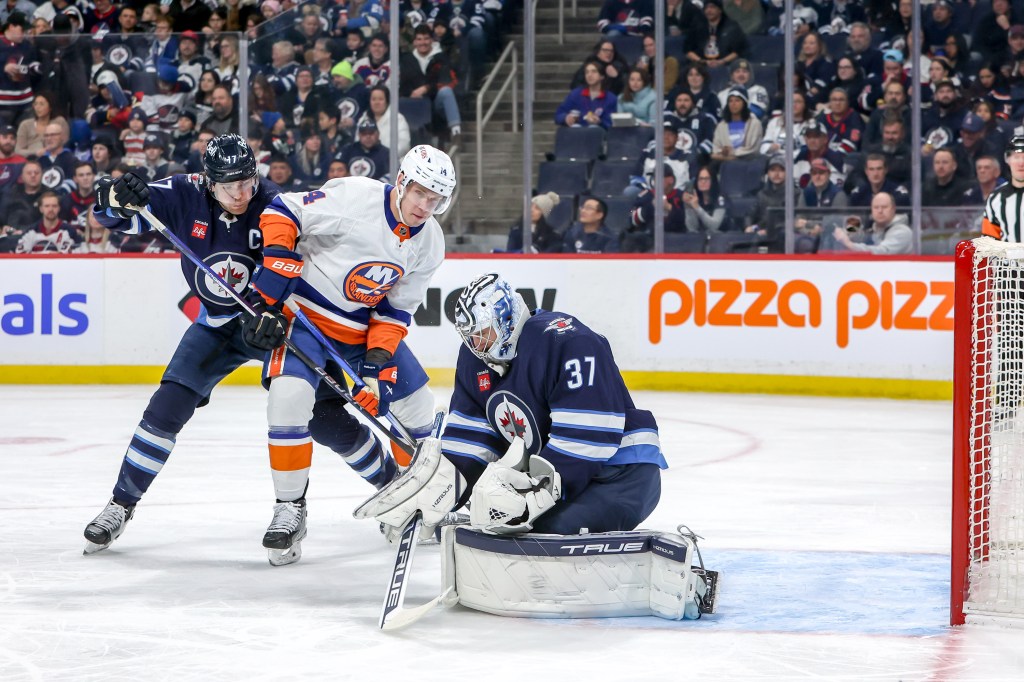 Goaltender Connor Hellebuyck #37 of the Winnipeg Jets makes a save as Adam Lowry #17 and Bo Horvat #14 of the New York Islanders battle.