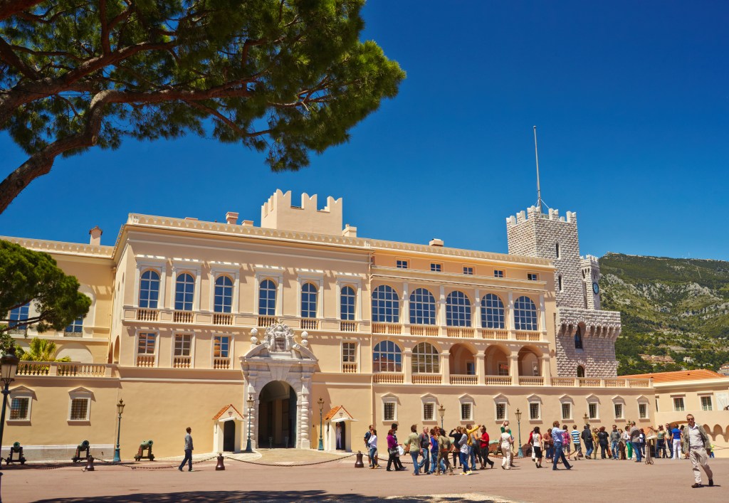 A photo of the front of the princely palace in Monaco, wit people walking in front