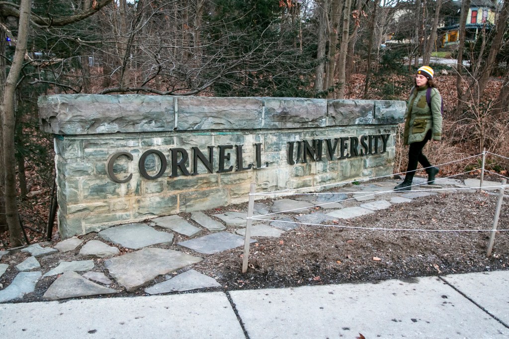 A Cornell University sign on the campus in Ithaca, New York, with a woman passing by.