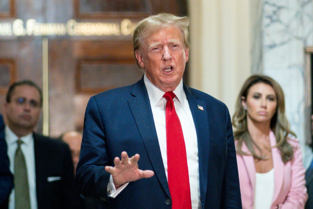 Donald Trump in a suit and tie, exiting a courtroom while being photographed by the press.