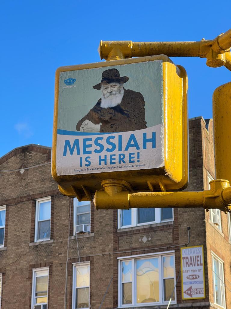 poster, showing an image of Lubavitcher Rebbe Menachem Mendel Schneerson and the words "Messia Is Here!" on a crosswalk sign