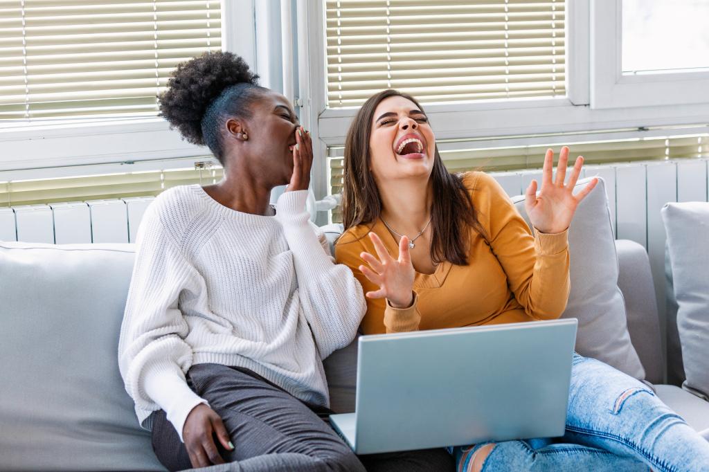 Girlfriend watching a very funny movie on laptop. Smiling young women relaxing and watching movies at home, female friends having rest after hard week, copy space