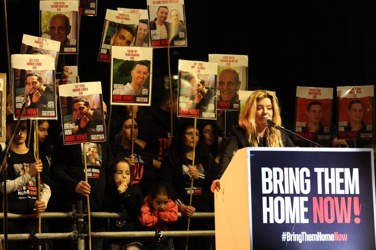 A woman delivers a speech as relatives and supporters hold placards bearing portraits of Israeli hostages held in Gaza since the October 7 attacks by Hamas in southern Israel, on the sidelines of a rally calling for their release, in Tel Aviv on January 6, 2024