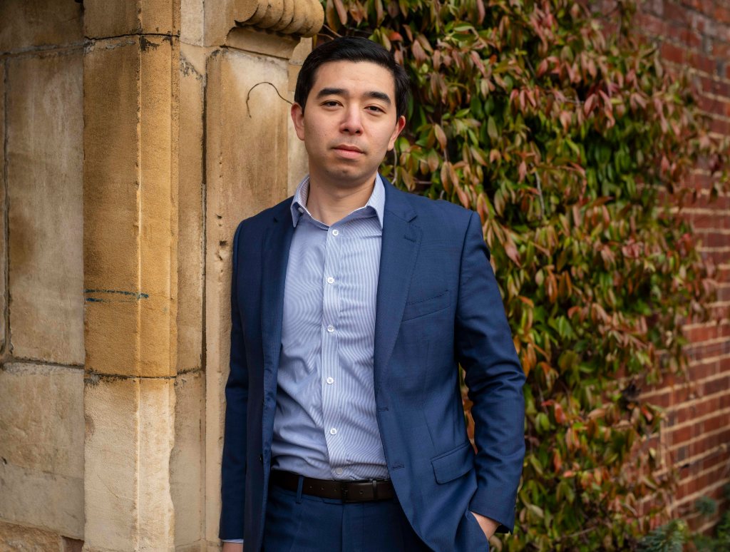 Rob Henderson leans against a wall outside at Cambridge campus.