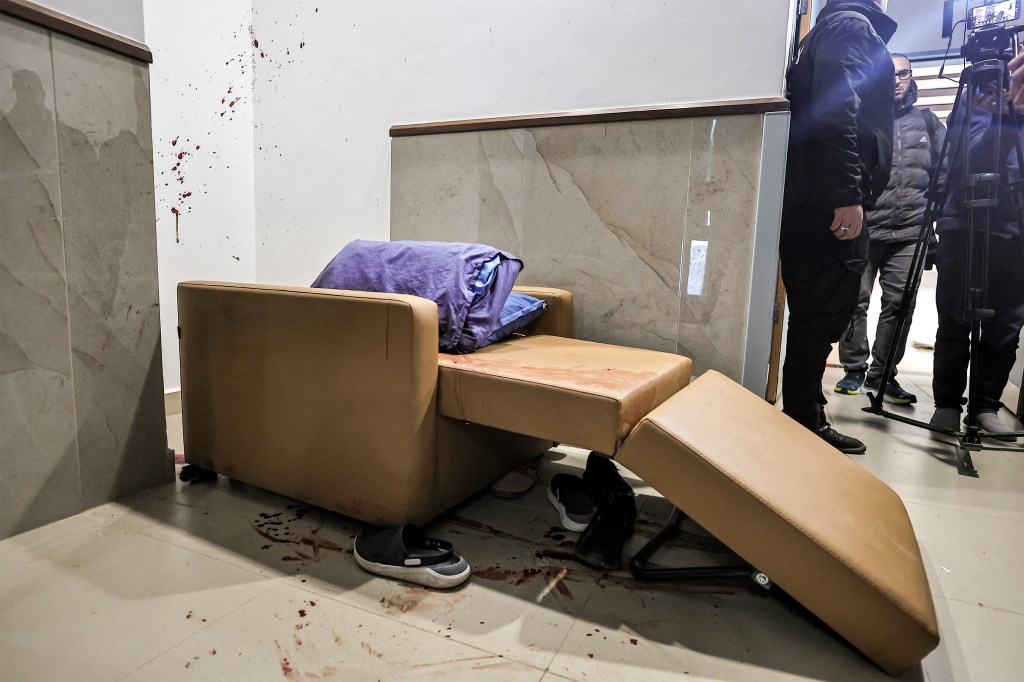 Blood stains are splattered on a wall and cover the floor by discarded shoes and clogs next to a chair at the Ibn Sina hospital in Jenin