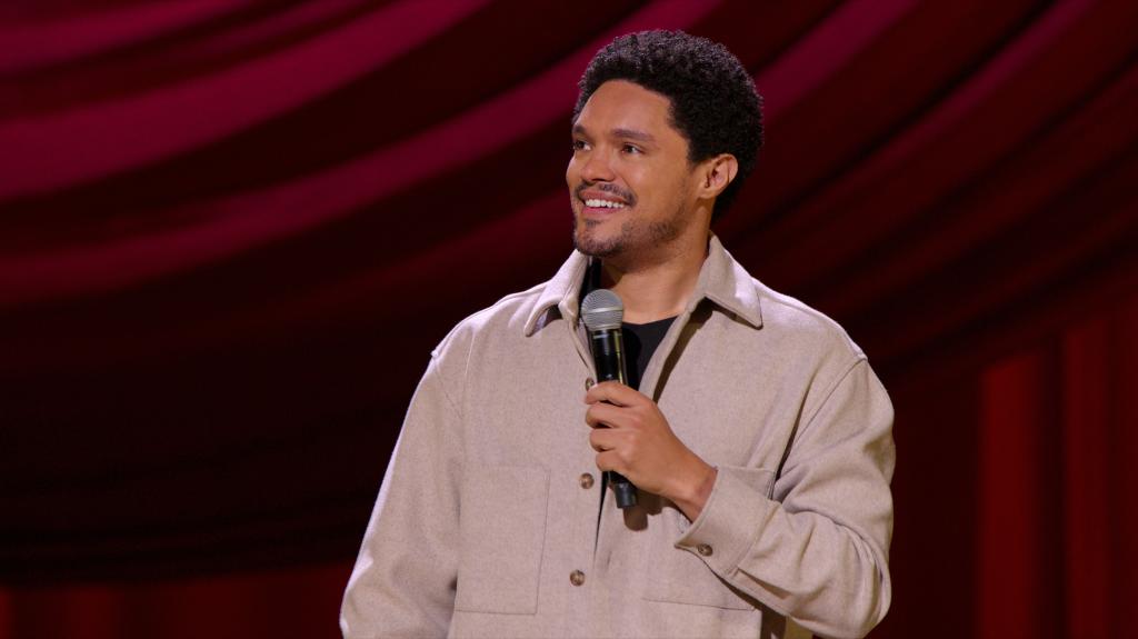 Trevor Noah standing onstage smiling. 