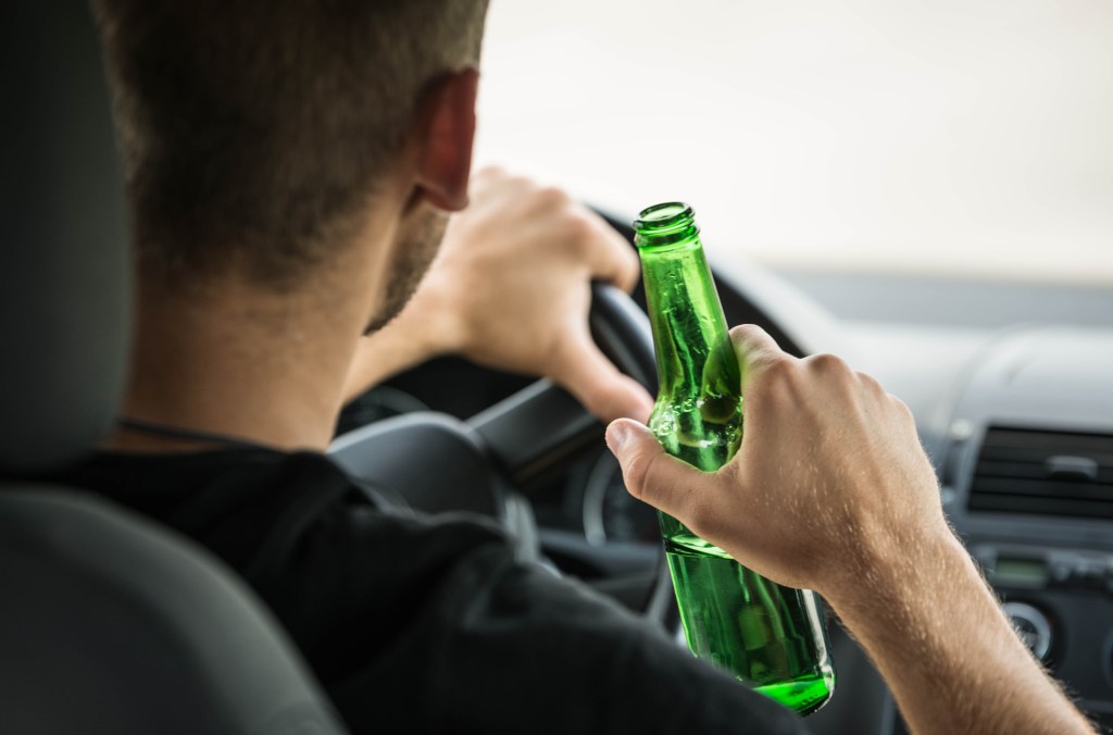 stock photo of man driving while drinking an unmarked beer 