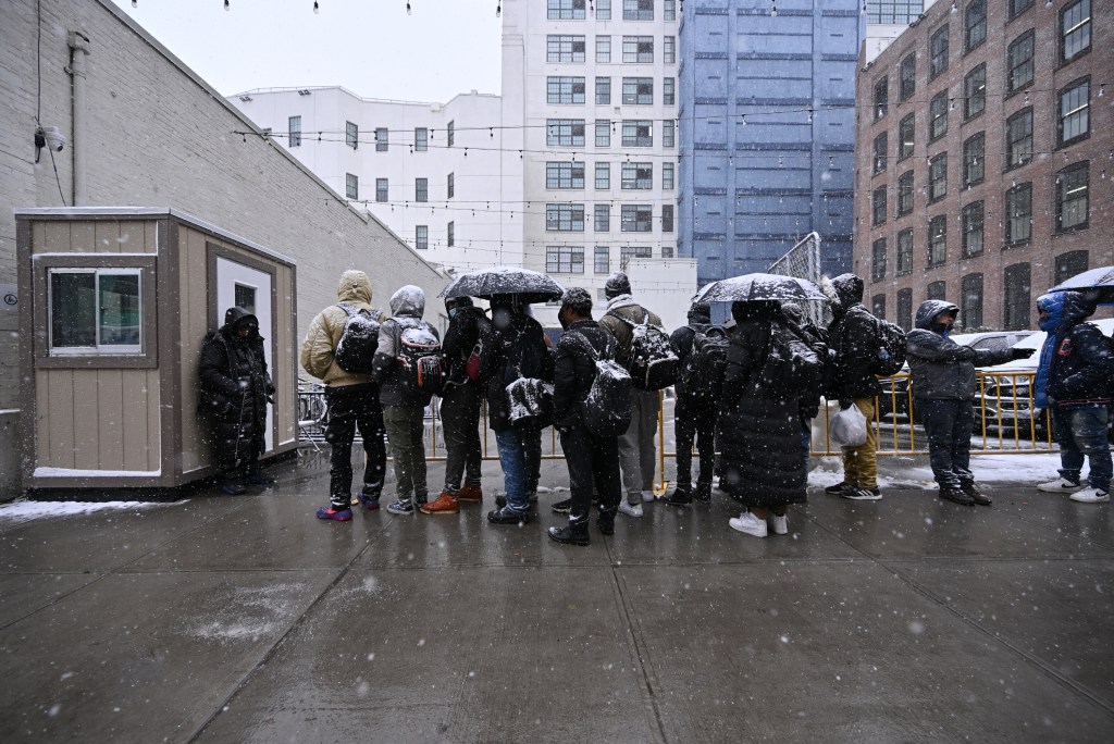 A group of migrants waits outside an intake center in Brooklyn in the snow.