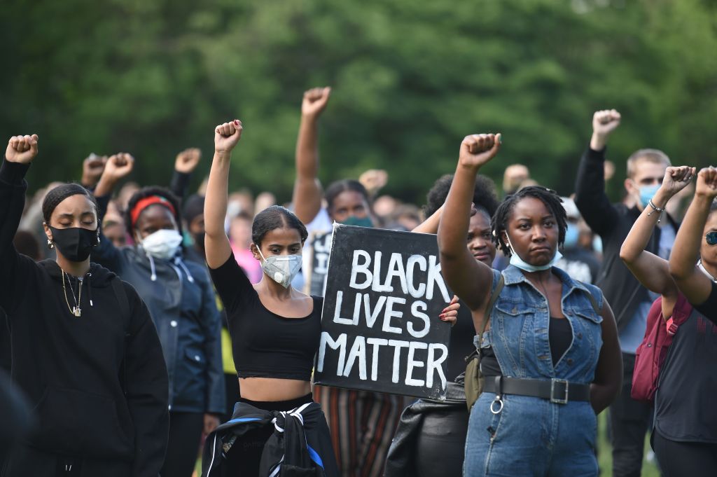 Black Lives Matter activists protest police violence. One holds a sign reading "Black Lives Matter" and several hold their fists in the air