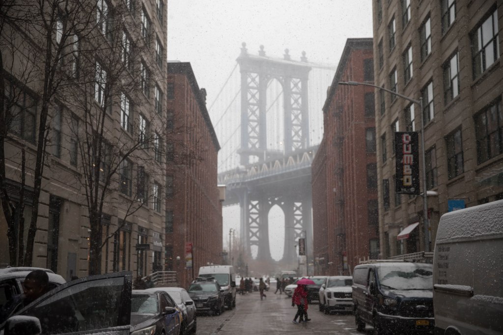 The Brooklyn Bridge appears hazy in the background as snow falls around New York City on Jan. 19, 2024.