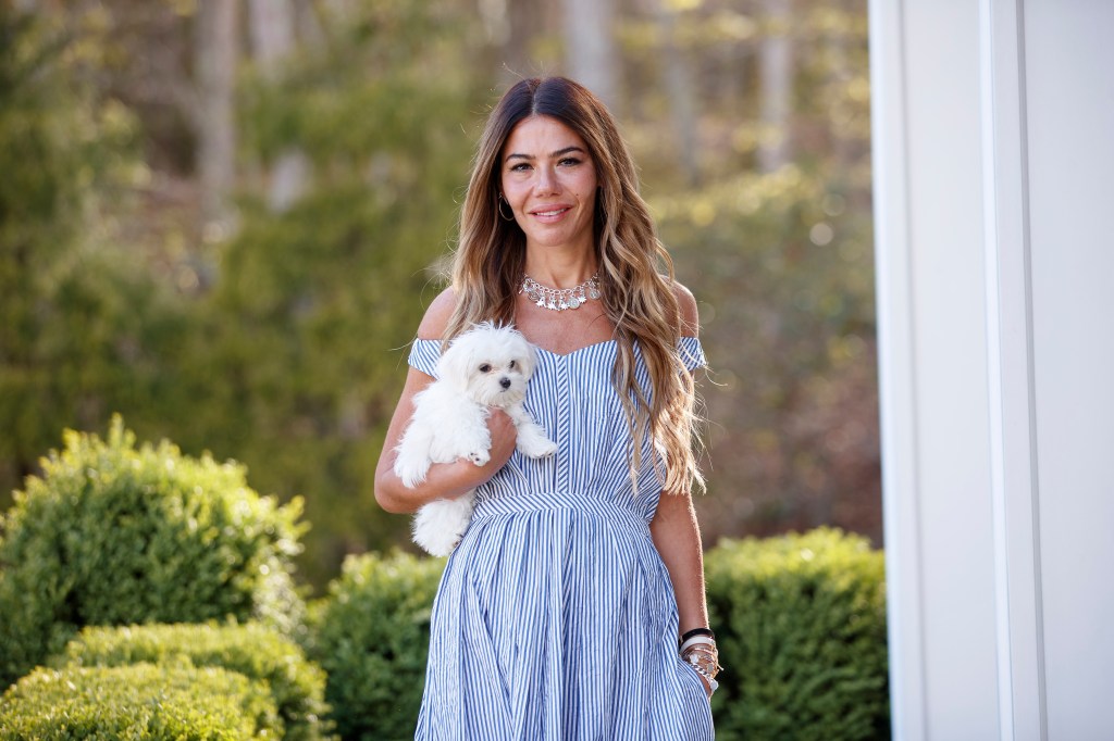 Libbie Mugrabi standing outdoors and holding a small white dog.