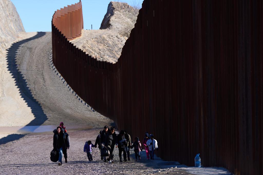 Migrants walk along the U.S.-Mexico border wall after crossing border