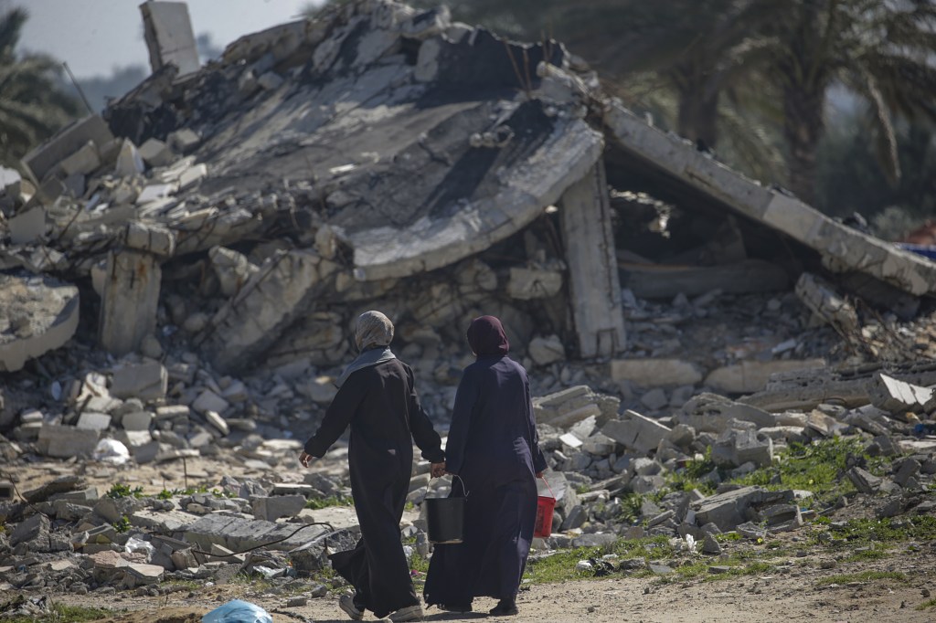 Displaced Palestinian women pass by a destroyed structure in Deir Al Balah, southern Gaza Strip, 14 February 2024. 