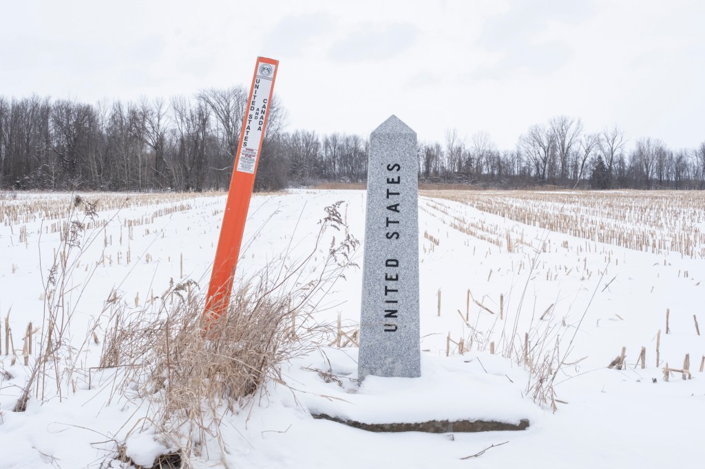 A cement obelisk reading "United States" stands in a snowy field next to an orange marker.