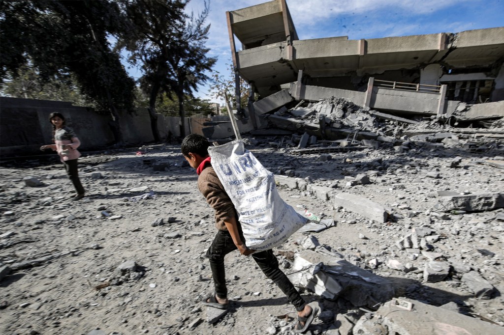 A boy carries a sack bearing the logo of the United Nations Relief and Works Agency for Palestine Refugees in the Near East (UNRWA), filled with salvaged items from the rubble of a destroyed highschool in the Nuseirat camp for Palestinian refugees, which was severely damaged by Israeli bombardment amid the ongoing conflict in the Gaza Strip between Israel and the Palestinian militant group Hamas, in the central Gaza Strip on February 1, 2024. (Photo by ANAS BABA / AFP) (Photo by ANAS BABA/AFP via Getty Images)