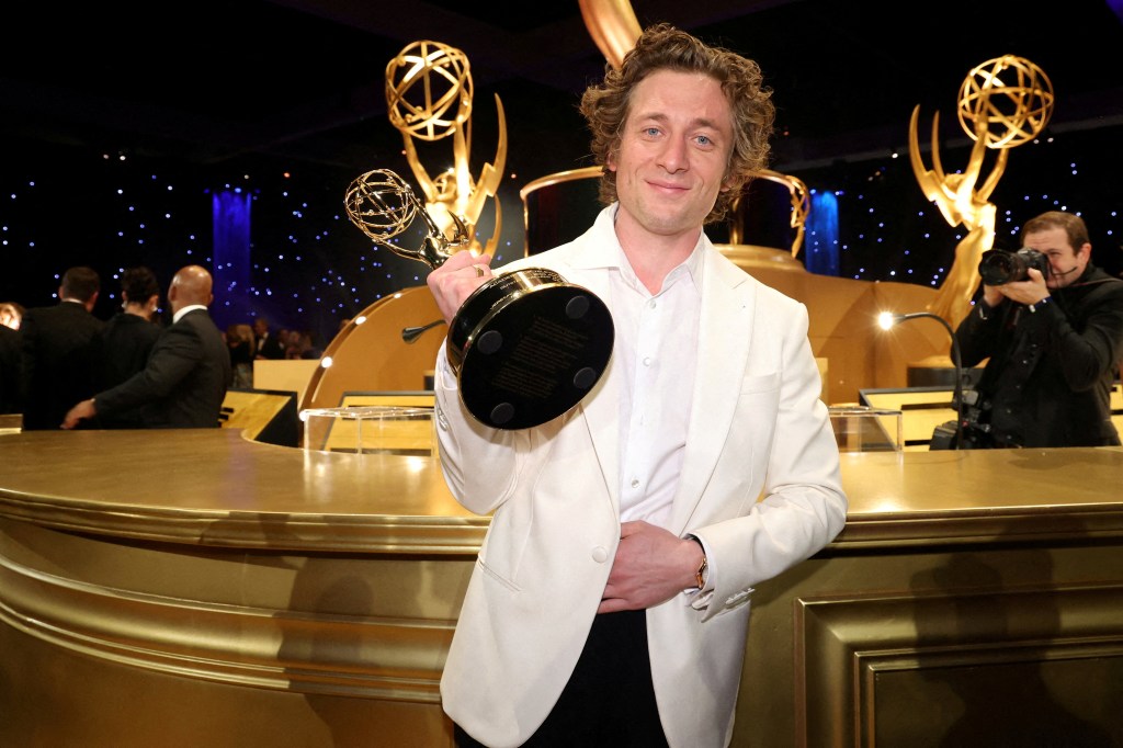 Jeremy Allen White smiling and holding up a Golden Globe. 