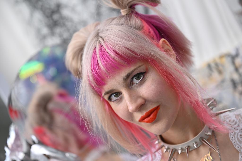 Julia Sinelnikova with pink hair and a spiked necklace standing in her studio.