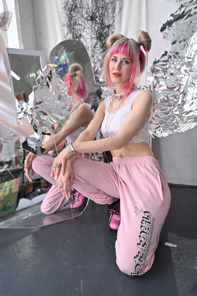 Julia Sinelnikova sitting on the floor with pink hair and pink pants.