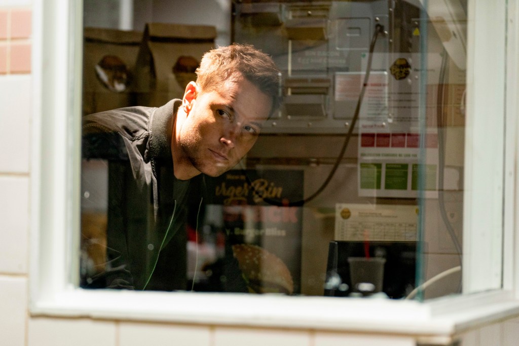 Justin Hartley looking out a window. 