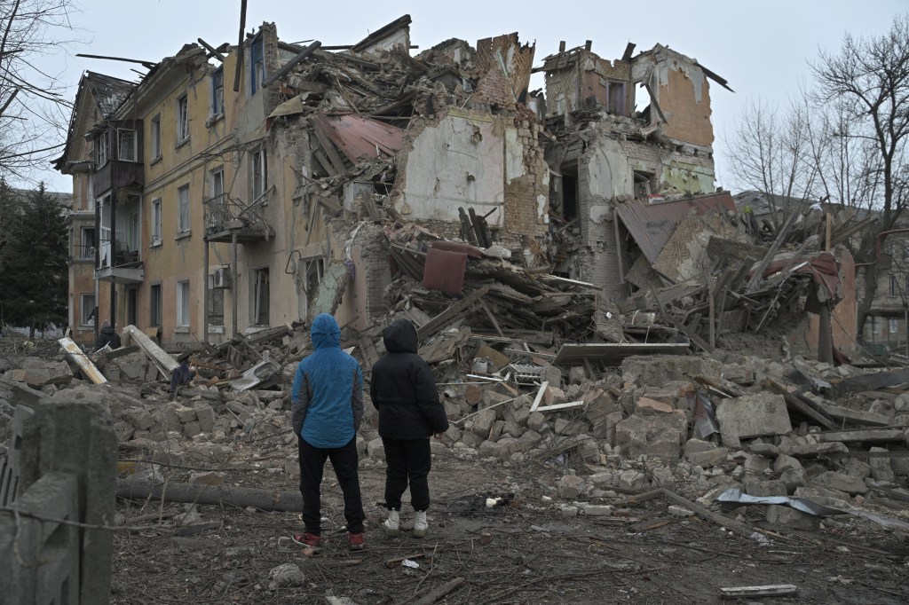 Local residents stand among debris of a residential building partially destroyed by a missile attack in the town of Selydove, Donetsk region, on February 8, 2024.