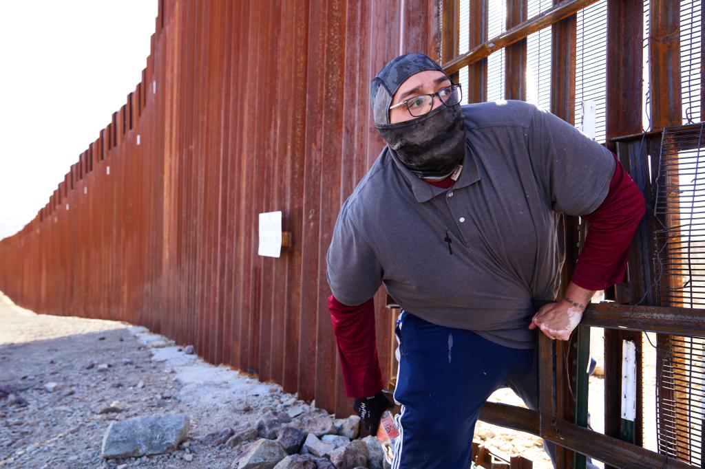 A migrant from Mexico who did not want to claim asylum squeezes through a gap in the U.S.-Mexico border wall