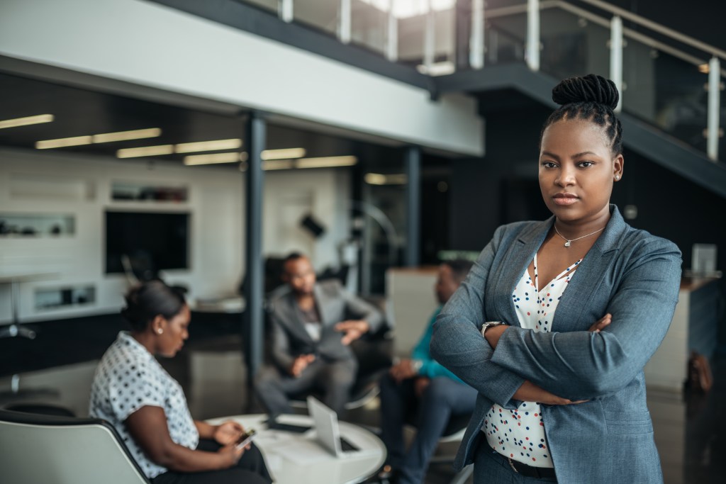 Portrait of a confident black businesswoman with crossed arms and an all-African team in the background