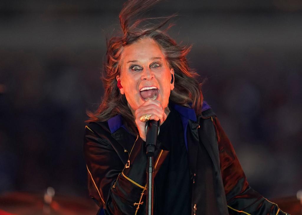 Ozzy Osbourne performing with a microphone on stage at a football game halftime show.