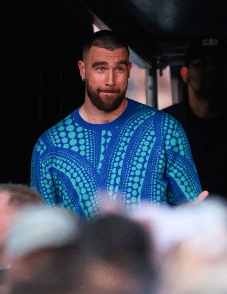 Travis Kelce, a man in a blue shirt, standing on a stage with fans in the background.