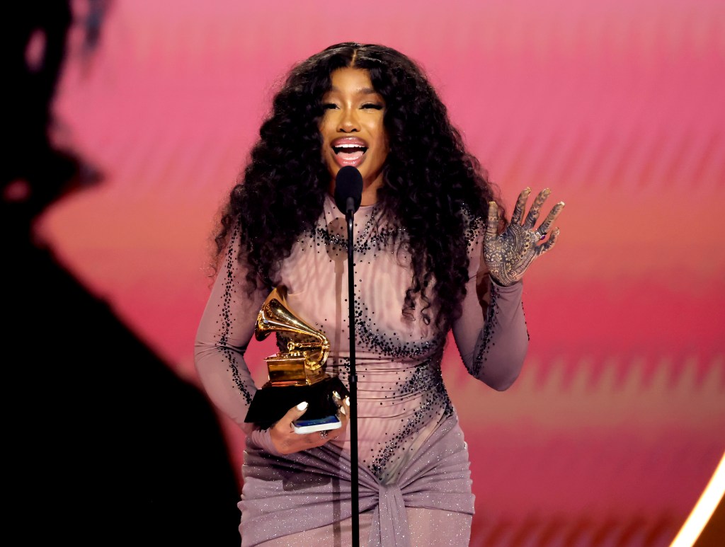 Picture of SZA holding Best R&B Song trophy with a microphone in front, onstage at GRAMMY Awards 66th show.