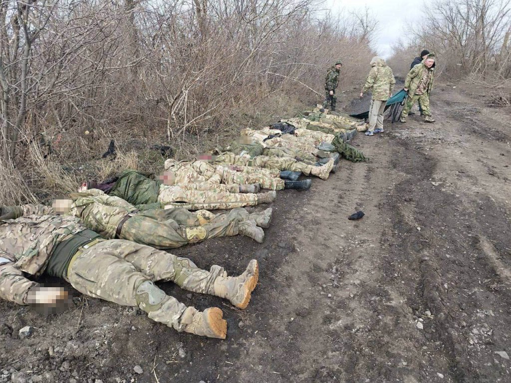 Survivors of the attack line up their dead comrades next to the tree line