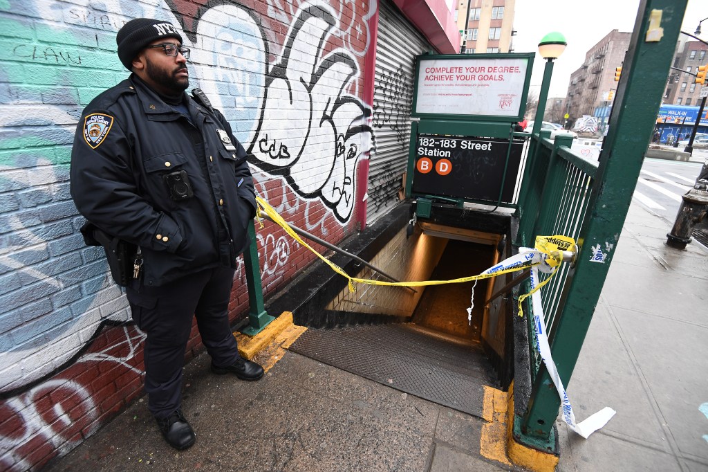 Police officers standing outside of subway station that has been taped off. 