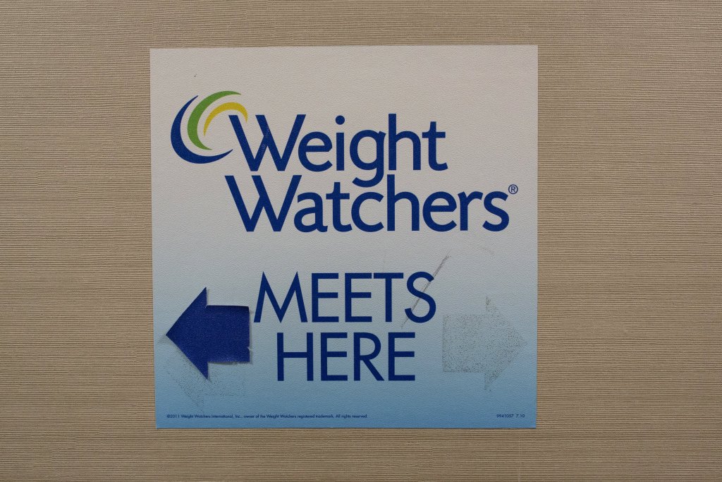 Sign for Weight Watchers displayed on a wall with no people, blue background and Weight Watchers text in the centre.