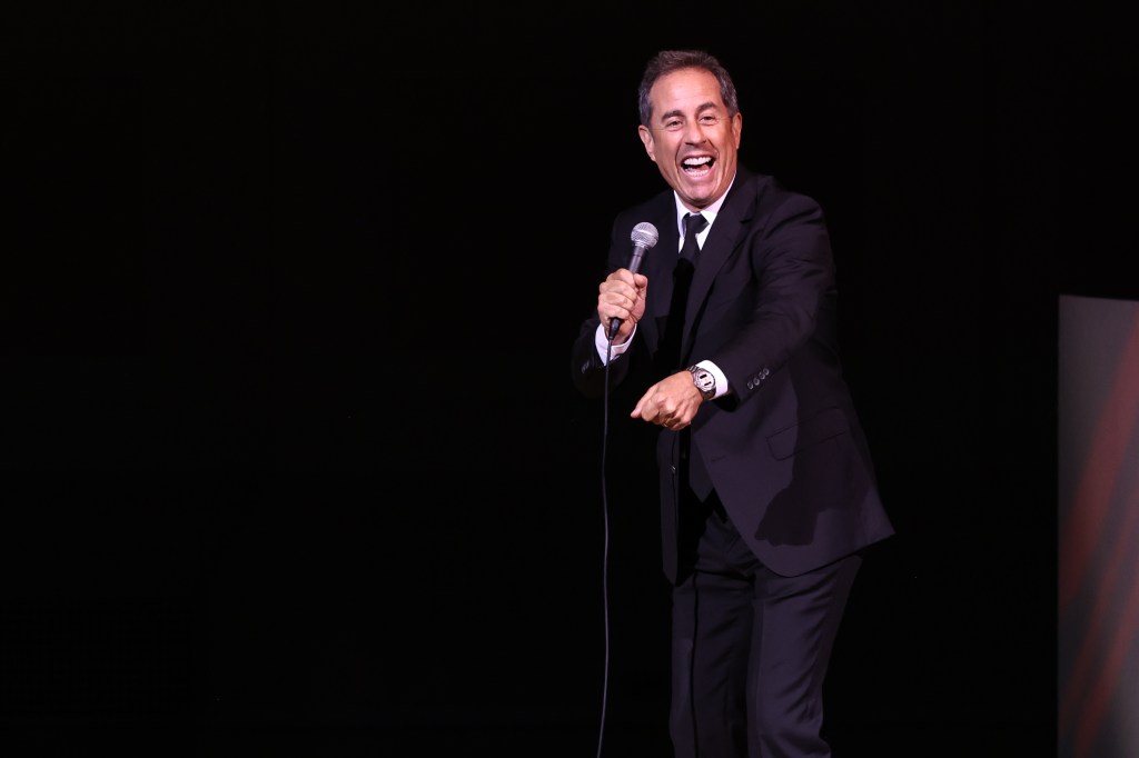 Jerry Seinfeld, dressed in a suit, performing on stage at the 2023 Good+Foundation benefit at Carnegie Hall, New York City