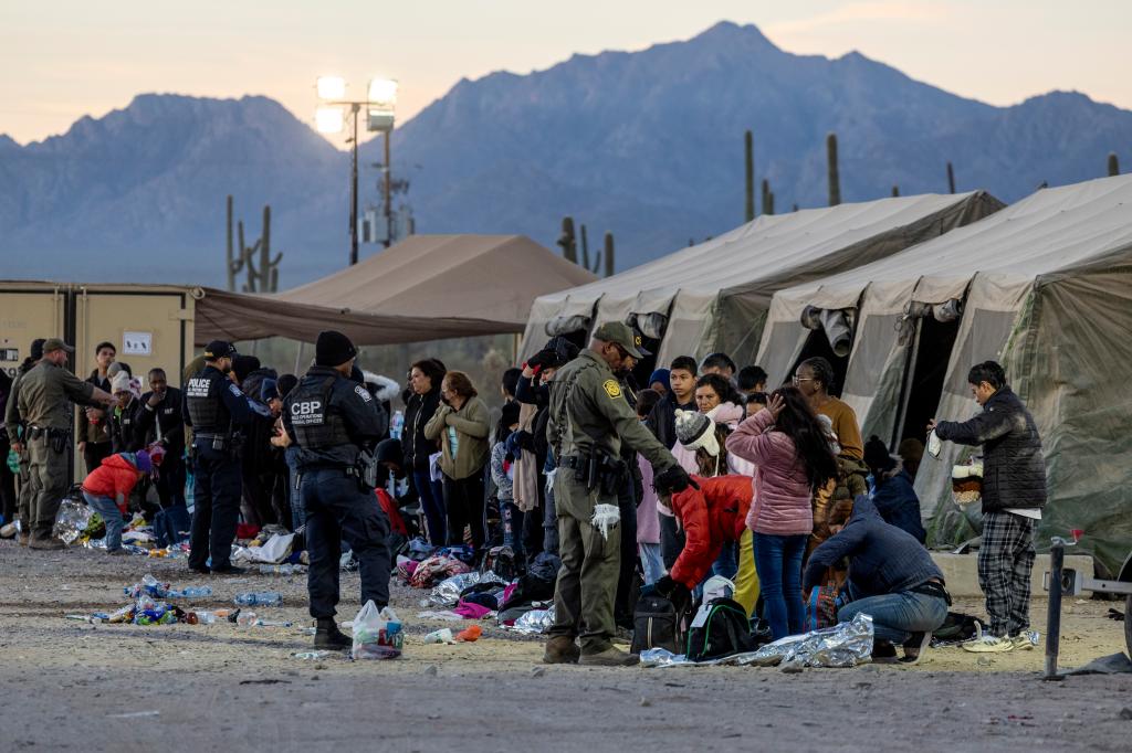 A line of people forms outside tents as U.S. Customs and Border Protection agents address immigrants at a processing center near the border.