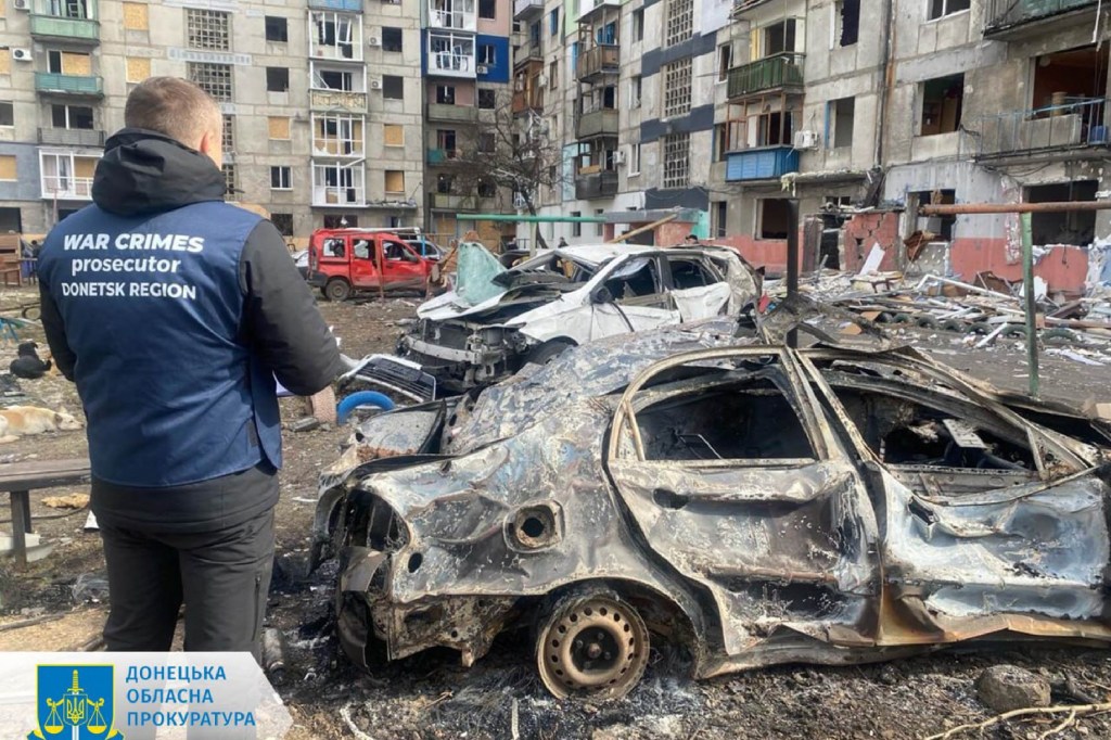 This handout photograph taken and released by Donetsk Region Prosecutor`s Office on March 10, 2024 shows a war crimes prosecutor standing next to destroyed cars in the courtyard of a damaged residential building following a missile attack in Myrnohrad, Donetsk region. A Russian night-time strike on the east Ukrainian town of Myrnograd wounded at least 11 people, Kyiv said on March 10, 2024.