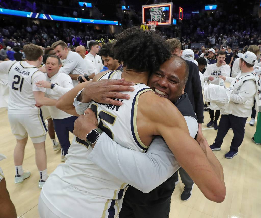 A group of people, including Akron Zips forward Enrique Freeman and Athletic Director Charles Guthrie, hug in celebration after winning the MAC Tournament championship game.