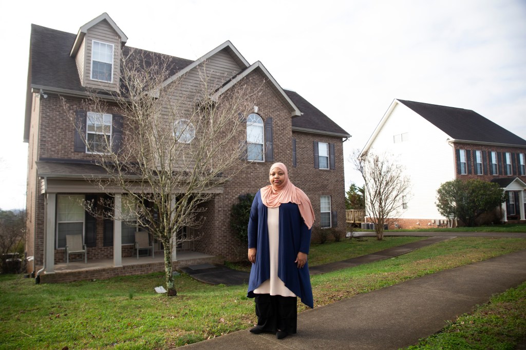 A woman stands outside a house, posing for a portrait.