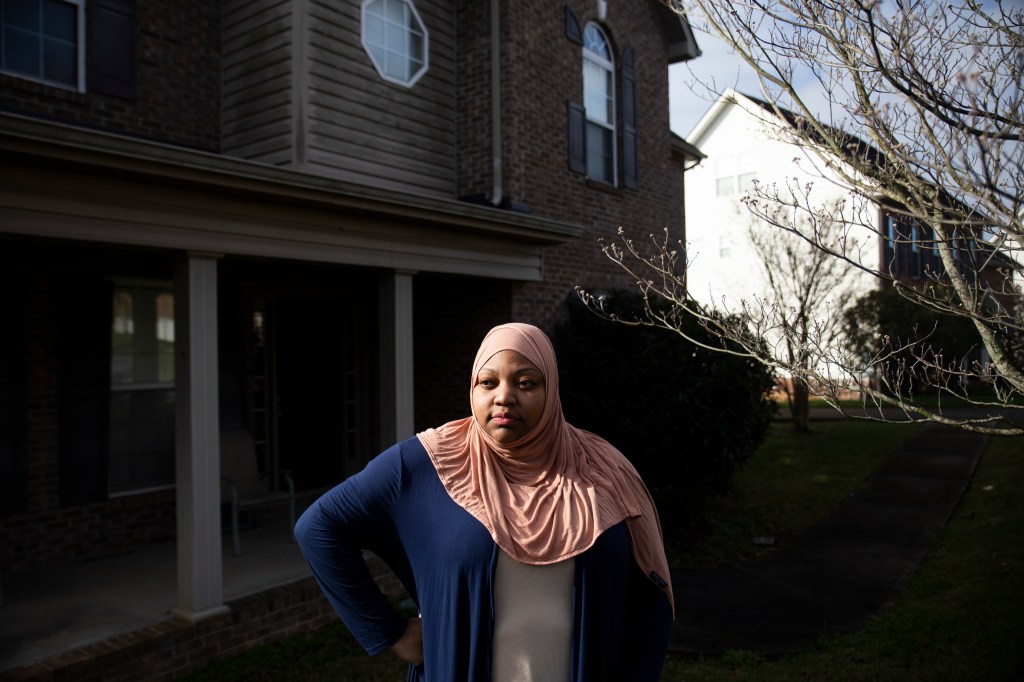 A woman in a blue and pink scarf standing in front of a house.