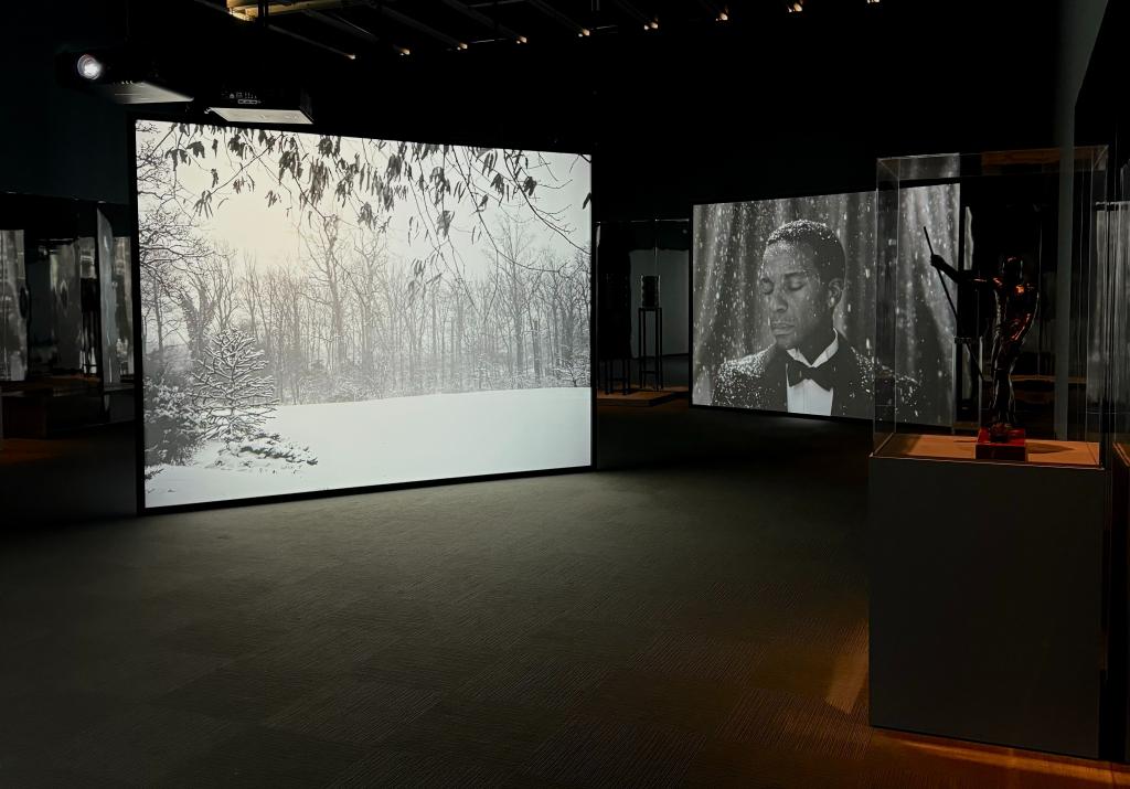 Installation view of Whitney Biennial 2024 exhibition at Whitney Museum, featuring large screens displaying art