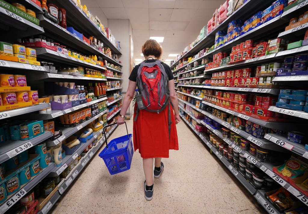 A shopper walking through the aisle of Tesco supermarket amidst shelves stocked with downscaled groceries.