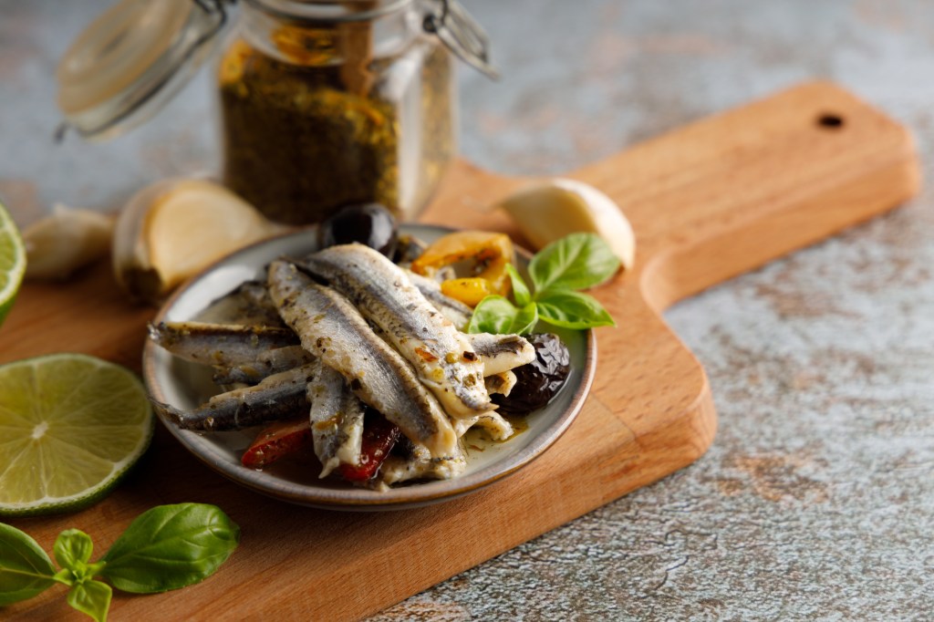 Mediterranean appetizer, anchovy fish in olive oil and herbs in a small bowl.