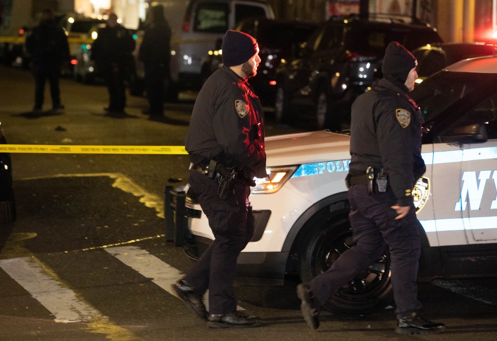 Police officers walk past a patrol car on a Queens street.