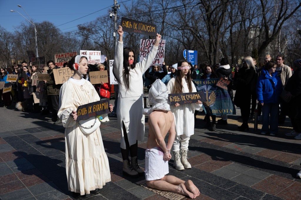 Protesters in white robes hold signs in a rally demanding the release of Azovstal plant defenders held captive in Russia.