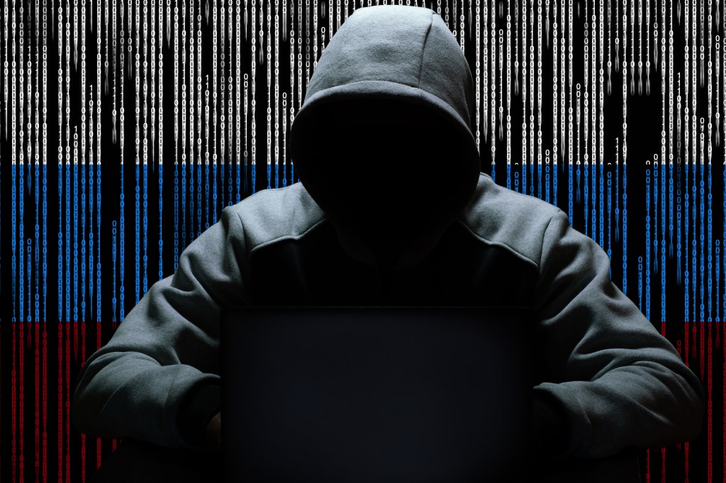 A hacker sitting with a hood against a backdrop of binary code. 