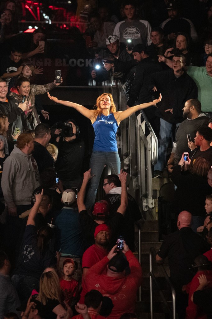 Lynch seen here in blue tank and black pants with her arms stretch out wide to the side as she stands amid a crowd, suffered a broken nose and concussion during a match. 