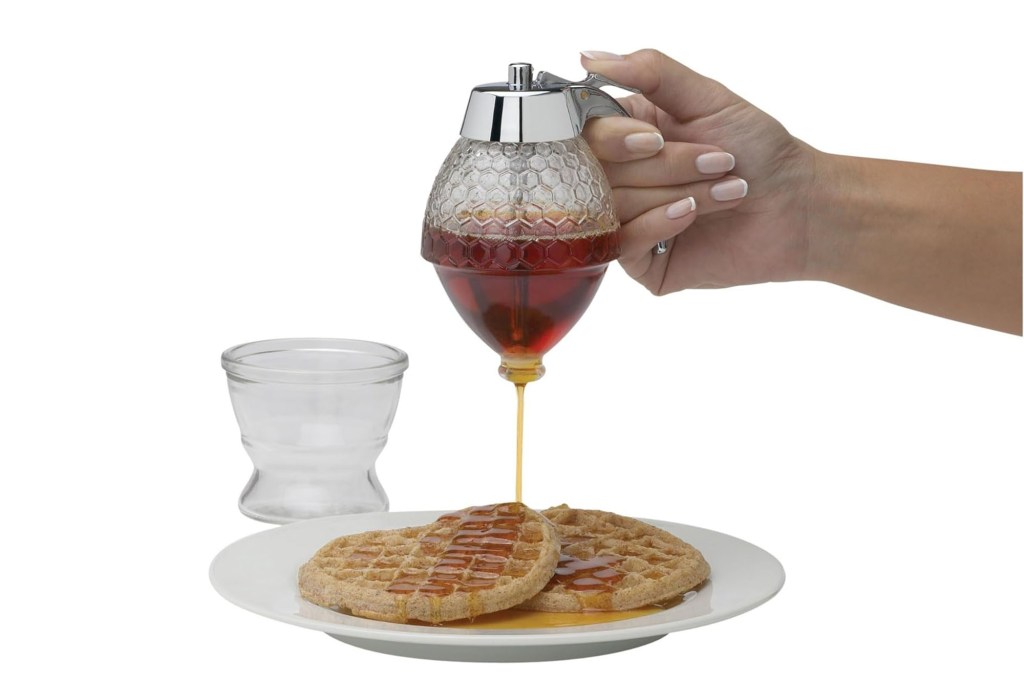 A hand pouring syrup into a waffle