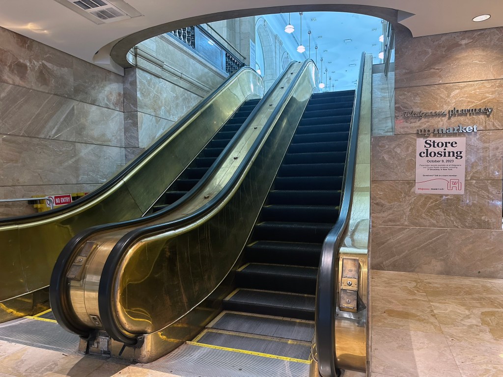 Gold escalators at 40 Wall Street with a "store closing" sign. 