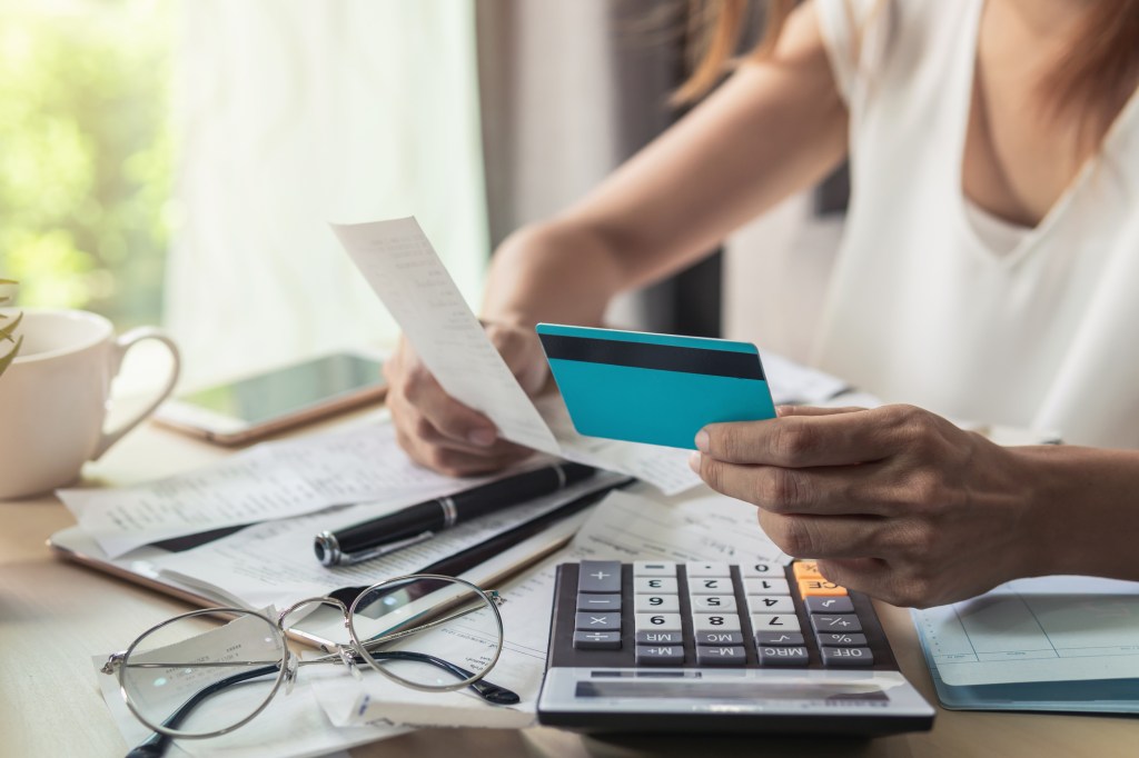 young woman checking bills and holding a credit card and paper at home